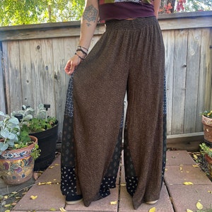 May include: Brown wide-leg pants with a black and white patterned trim. The pants have a high waist and a relaxed fit.