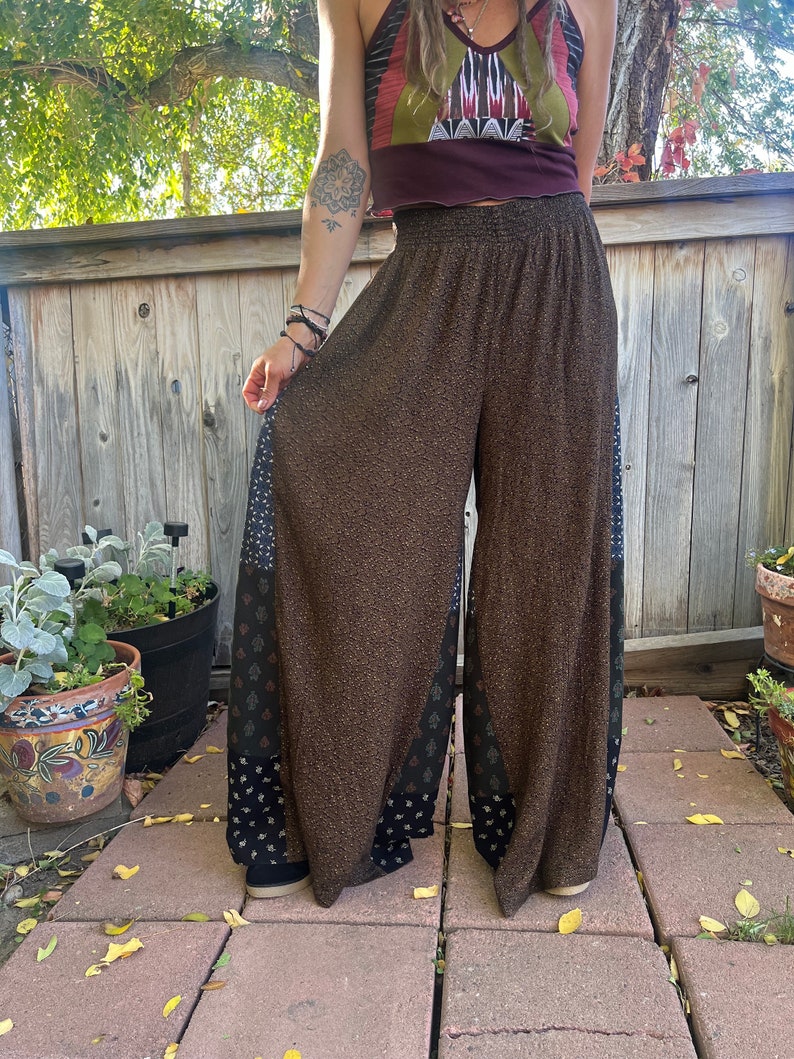 May include: Brown wide-leg pants with a black and white patterned trim. The pants have a high waist and a relaxed fit.