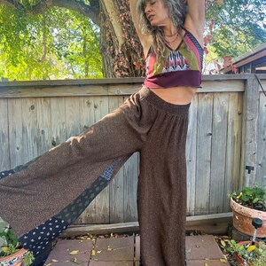 May include: A woman wearing a brown, patterned, wide-leg pants with a burgundy, green, and white patterned tank top. The pants have a patchwork design with black and white accents.