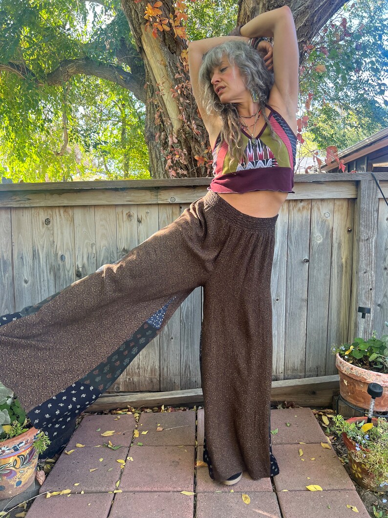 May include: A woman wearing a brown, patterned, wide-leg pants with a burgundy, green, and white patterned tank top. The pants have a patchwork design with black and white accents.