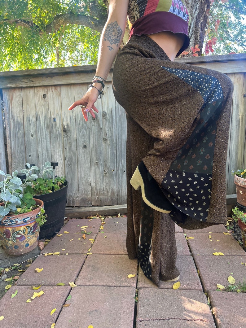 May include: Brown wide-leg pants with a black and white floral pattern on the side. The pants are made of a soft, flowing fabric and have a relaxed fit.