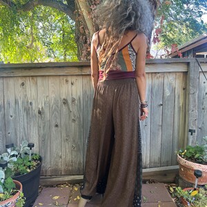 May include: Brown wide-leg pants with a black and white patterned side panel. The pants are made of a soft, flowing fabric and have a relaxed fit.