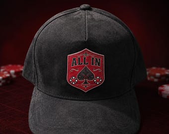 May include: A dark gray baseball cap featuring a red shield-shaped patch on the front. The patch displays the text ALL IN above a black spade symbol and two small poker chips. The text PREMIUM POKER HAT appears above the cap and AVAILABLE NOW below.