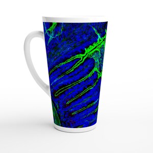 Puede incluir: Una taza de café con leche de cerámica blanca con un diseño abstracto vibrante. El diseño presenta un fondo azul con patrones verdes y negros en forma de venas. La taza tiene una forma alta y cónica y un asa curva.