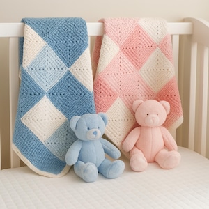 May include: Two baby blankets, one blue and white, the other pink and white, are draped over a white cot rail. Two plush teddy bears, one blue and one pink, sit on the cot mattress. The blankets have a diamond pattern.