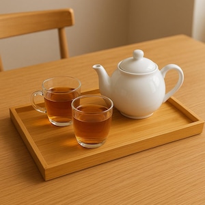 Peut inclure: Une théière en céramique blanche avec un couvercle et une poignée est posée sur un plateau en bois brun clair. Deux tasses en verre transparent et un verre de thé sont également sur le plateau.