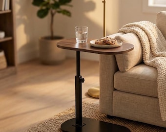 Può includere: Un tavolino laterale regolabile marrone scuro con base e stelo neri. Un bicchiere d'acqua e un piatto di biscotti sono sul piano del tavolo. Il tavolo è accanto a un divano beige con una coperta color crema.