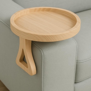 Könnte beinhalten: Ein helles Holz-Sofa-Armtablett mit runder Oberfläche und geschwungener Stütze. Das Tablett ist so konzipiert, dass es auf der Armlehne eines Sofas aufliegt und eine praktische Oberfläche bietet. Das Tablett hat einen Durchmesser von ca. 30 cm.