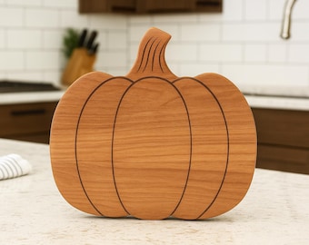 May include: A wooden pumpkin-shaped cutting board with a natural wood grain finish. The board features etched lines to define the pumpkin's sections and stem. Ideal for fall-themed kitchen decor and food preparation.
