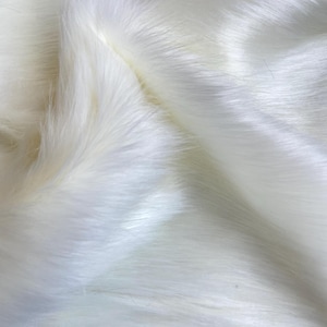 May include: White faux fur fabric with a soft, fluffy texture. The fur is arranged in a flowing, wavy pattern.