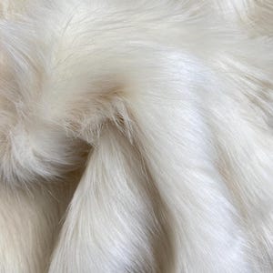 May include: Close-up of a white faux fur fabric. The fur is soft and fluffy, with a subtle sheen.