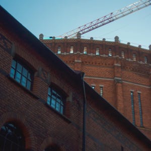 Puede incluir: Un edificio de ladrillo rojo con una gran estructura redonda de ladrillo en la parte superior. Una gr&uacute;a blanca y roja es visible en el cielo sobre el edificio.