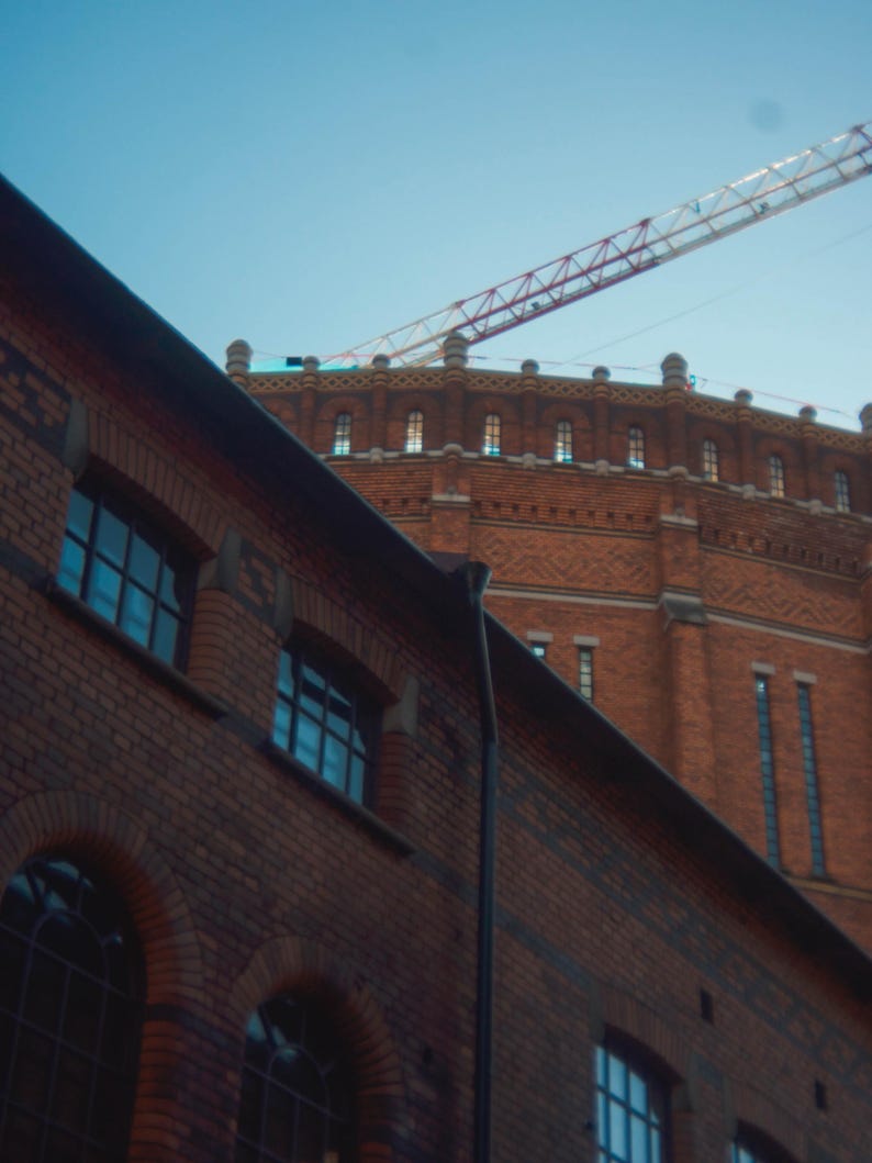 Puede incluir: Un edificio de ladrillo rojo con una gran estructura redonda de ladrillo en la parte superior. Una gr&uacute;a blanca y roja es visible en el cielo sobre el edificio.