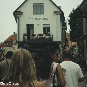 Op de afbeelding: Een straatbeeld met een menigte mensen die lopen. Een wit gebouw met de tekst "g:a masters" op de achtergrond. De afbeelding is gelabeld "shot with DejaDispo".