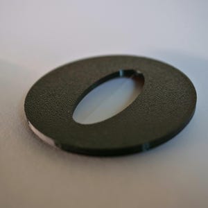 May include: A dark green, circular object with an oval-shaped cutout in the center. The object has a textured surface and a white interior visible through the opening. The edges are smooth and the object is set against a white background.
