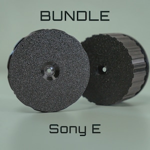 Op de afbeelding: Twee donkergrijze, cirkelvormige objecten met een textuur en een centraal gat. Het woord "BUNDLE" staat bovenaan en "Sony E" onderaan. De objecten lijken componenten of accessoires te zijn.