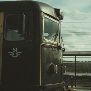 May include: A black train engine with a white "SJ" logo on the side. The engine has a large window and a yellow stripe running along the side.
