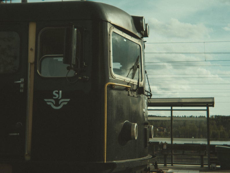 May include: A black train engine with a white "SJ" logo on the side. The engine has a large window and a yellow stripe running along the side.