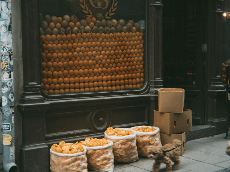 Puede incluir: Un escaparate de tienda con una gran pared de naranjas detr&aacute;s de un mostrador de madera. Hay varias cajas apiladas delante del mostrador.