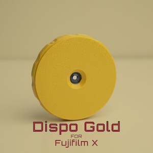 Puede incluir: Un accesorio de cámara amarillo Dispo Gold para cámaras Fujifilm X. El accesorio es circular con una superficie texturizada y un pequeño centro azul oscuro. El texto "Dispo Gold for Fujifilm X" se muestra en rojo.