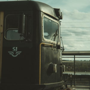 Może przedstawiać: Czarny lokomotywa z białym logo "SJ" na boku. Lokomotywa ma duże okno i ż&oacute;łty pasek biegnący wzdłuż boku.
