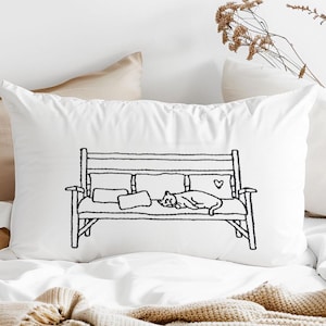 Op de afbeelding: Wit rechthoekig kussen met een zwarte lijntekening van een bank, kussens en een kat. De kat ligt op de bank. Op de achterkant van de bank is een hart getekend.