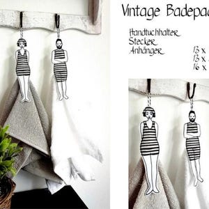 Op de afbeelding: Vintage badhanddoekhouderset met twee zwart-wit illustraties van mensen in badpakken. De set bevat een handdoekhouder, een sticker en een hanger. De afmetingen zijn 13 x 18 inch, 13 x 23 inch en 16 x 26 inch.