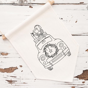 Può includere: Striscione color crema con un disegno ricamato nero di un'auto d'epoca che trasporta regali e una ghirlanda. Lo striscione è appeso con tasselli di legno e spago, perfetto per le decorazioni natalizie.