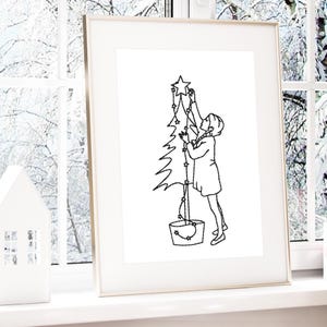 Könnte beinhalten: Eine gerahmte Schwarz-Weiß-Strichzeichnung zeigt eine Person, die einen Weihnachtsbaum mit sternförmigen Lichtern schmückt. Das Kunstwerk ist vor einem verschneiten Fensterhintergrund platziert, mit einer kleinen weißen Hausfigur im Vordergrund.