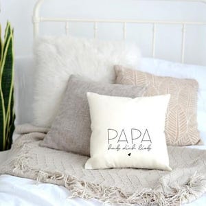 Puede incluir: Almohada blanca con texto negro que dice "PAPA hab dich lieb" con un pequeño corazón negro.