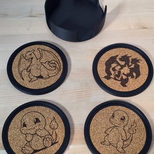 May include: Set of four round coasters with black rims and cork centers, each featuring a different engraved Pokémon design. A matching black coaster holder is also included. The coasters are designed for use with cups and glasses.