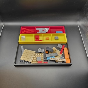 May include: A black plastic organizer tray with red, yellow, and black compartments. The compartments contain various colorful toy building blocks. The tray is designed to sort and store the blocks, keeping them organized and accessible.