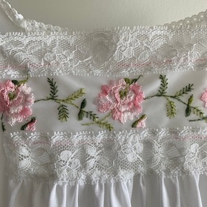 Puede incluir: Borde de encaje blanco con flores bordadas en rosa y verde.