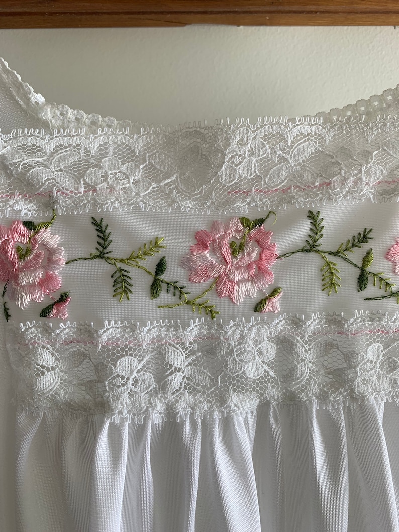 Puede incluir: Borde de encaje blanco con flores bordadas en rosa y verde.