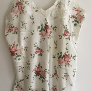 May include: A white satin slip with a floral print featuring pink and red roses. The slip has thin straps and a scalloped neckline.