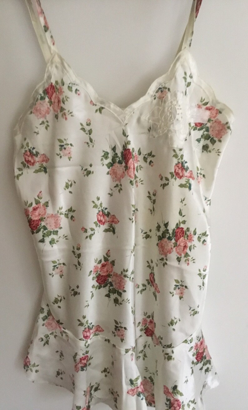 May include: A white satin slip with a floral print featuring pink and red roses. The slip has thin straps and a scalloped neckline.
