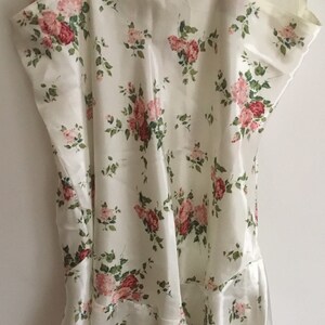 May include: A white satin slip with a floral pattern featuring pink and red roses. The slip has thin straps and a scalloped neckline.
