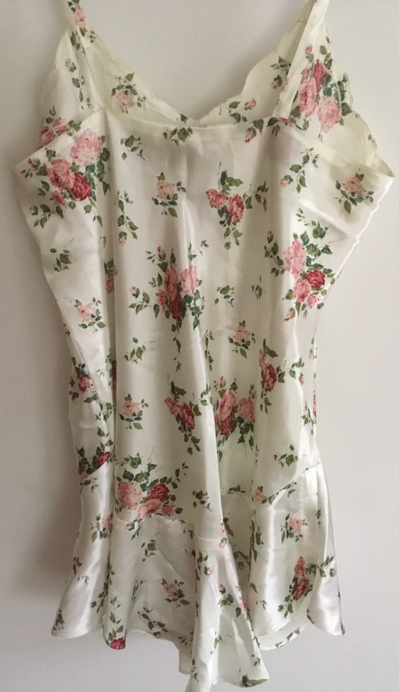 May include: A white satin slip with a floral pattern featuring pink and red roses. The slip has thin straps and a scalloped neckline.