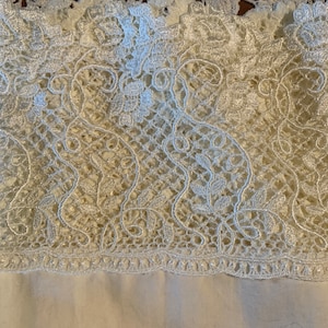 May include: White lace trim with a delicate floral pattern. The lace is made of a fine, lightweight material and has a soft, flowing texture.