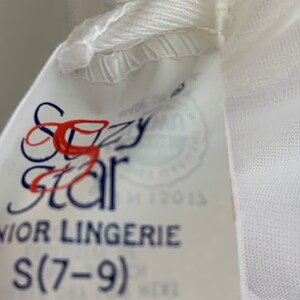 Puede incluir: Etiqueta blanca con texto azul y rojo que dice "Sizzy Star Junior Lingerie S(7-9)"