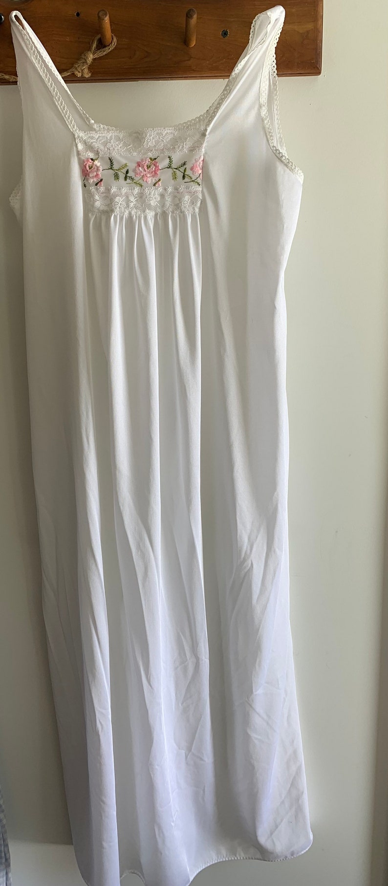 Puede incluir: Un camis&oacute;n blanco de algod&oacute;n con delicado encaje y bordado floral rosa. Las tiras son finas y ajustables.