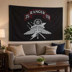 May include: A black rectangular wall tapestry featuring the 75th Ranger Regiment Special Troops Battalion emblem in white and grey. The design includes a central star, wings, a parachute, a dagger, and a banner with the text 75 RANGER STB.