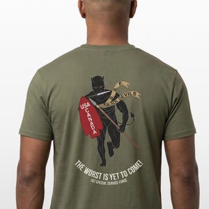 May include: Olive green t-shirt featuring a black devil graphic with a spear and shield. The shield reads "USA CANADA." A banner above the devil reads "BLACK DEVILS." The text "THE WORST IS YET TO COME!" and "1ST SPECIAL SERVICE FORCE" are below the graphic.