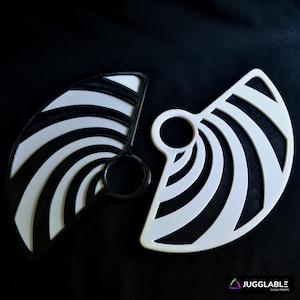 May include: Two fan-shaped props, one black and white, the other white. Each has a handle and curved stripes. The props are set against a black background. The text "JUGGLABLE FLOW PROPS" is in the bottom right corner.