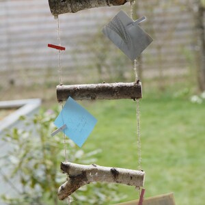 Puede incluir: Un tablero de notas de madera rústico con cuerda y pinzas para la ropa colgando de la parte superior. Tiene tres trozos de papel con notas escritas a mano y una tarjeta en blanco adjunta.