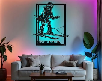 Op de afbeelding: Zwart metalen wandkunstwerk dat een skiër in actie afbeeldt, omlijst door een rechthoekige rand. Het kunstwerk bevat de tekst "CUSTOM NAME" aan de onderkant. De skiër draagt een helm en ski's, en het stuk is op een witte muur gemonteerd.