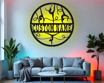 May include: A black metal wall art piece featuring gymnast silhouettes within a circular frame. The text "CUSTOM NAME" is displayed prominently. The artwork is illuminated with a yellow glow, creating a striking visual effect.