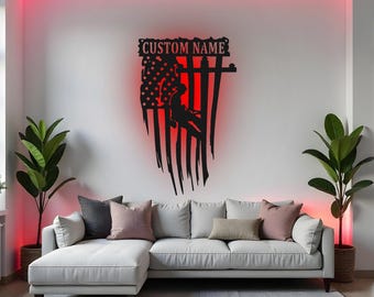 May include: A black metal wall art piece depicting an American flag with a firefighter silhouette and the text "CUSTOM NAME". The flag design has a red illuminated background, and is mounted above a white couch with decorative pillows.