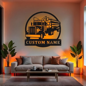 Pode incluir: Arte de parede em metal preto de um caminhão transportando toras, emoldurado em um círculo. O texto "CUSTOM NAME" é exibido em uma placa retangular abaixo do caminhão. A obra de arte é iluminada com luz quente.
