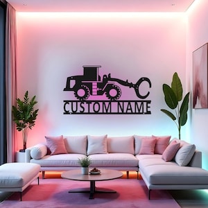 Pode incluir: Arte de parede em metal preto com um skidder de toras estilizado com o texto "CUSTOM NAME" abaixo. A obra de arte é montada em uma parede branca acima de um sofá moderno com almofadas rosa. O quarto tem um esquema de cores rosa e roxo.